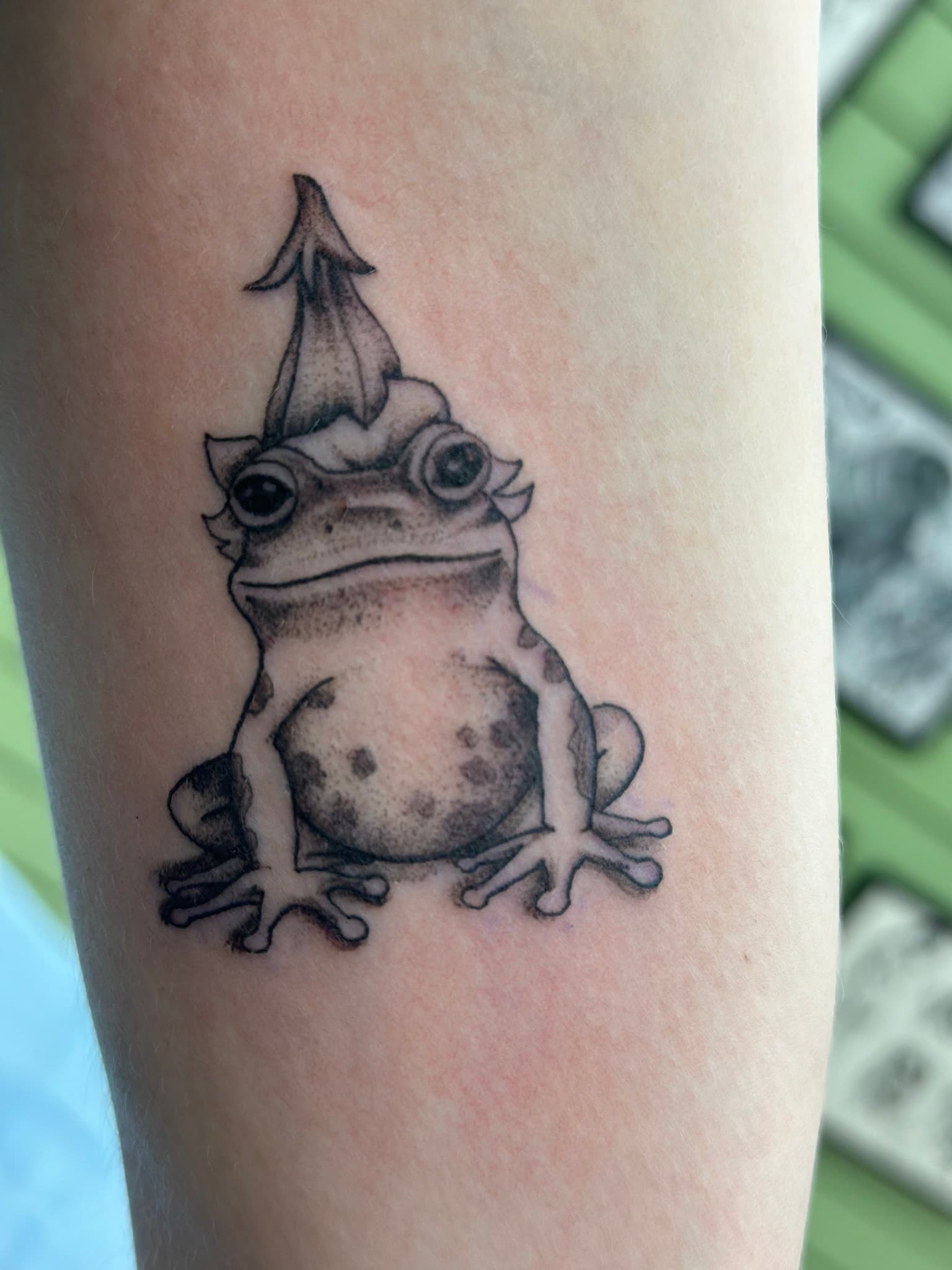 Fine line frog wearing a flower hat tattoo by Isaac Mackenzie