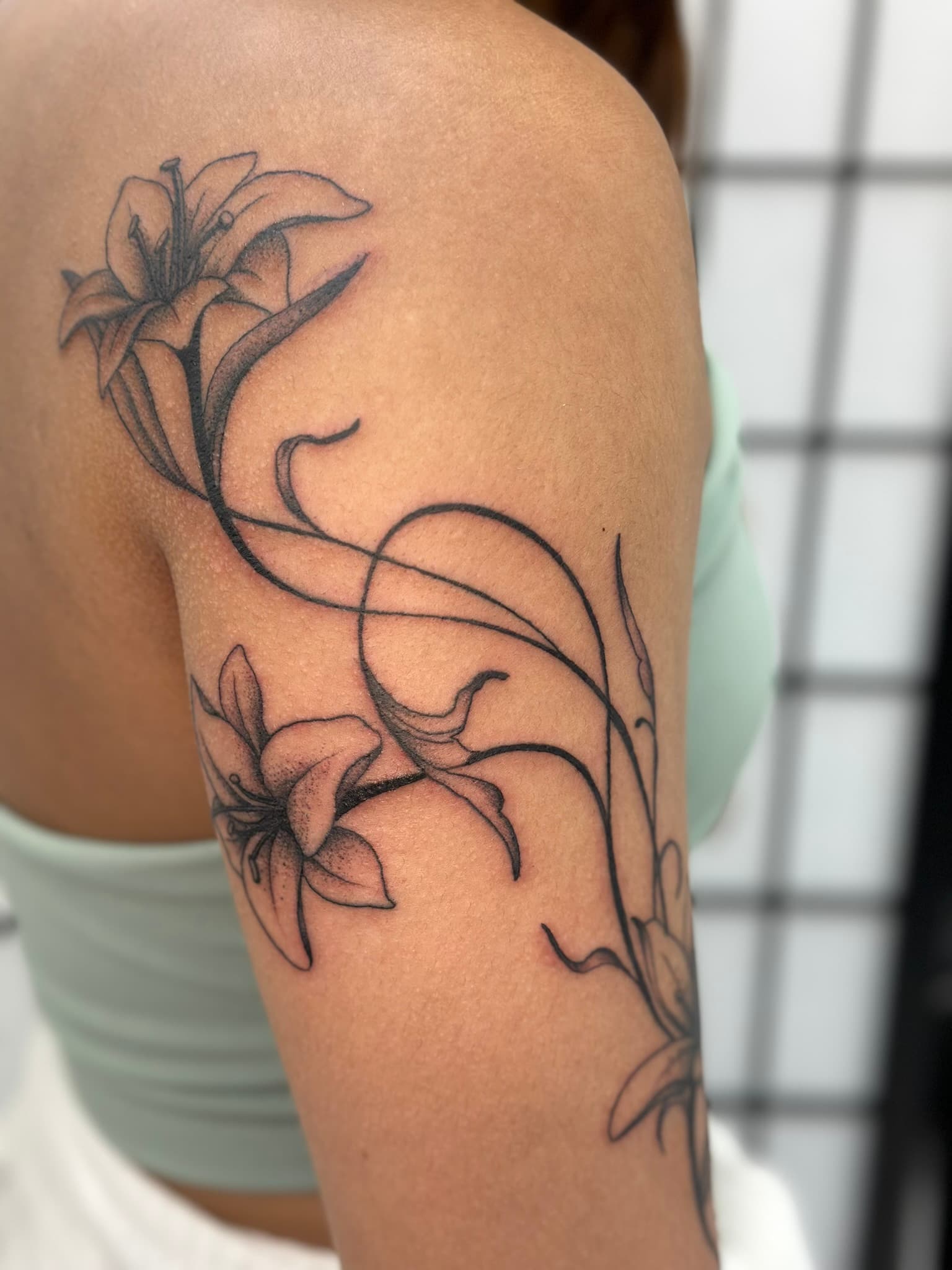 Fine line whimsical arm lilies tattoo by Isaac Mackenzie, Oahu