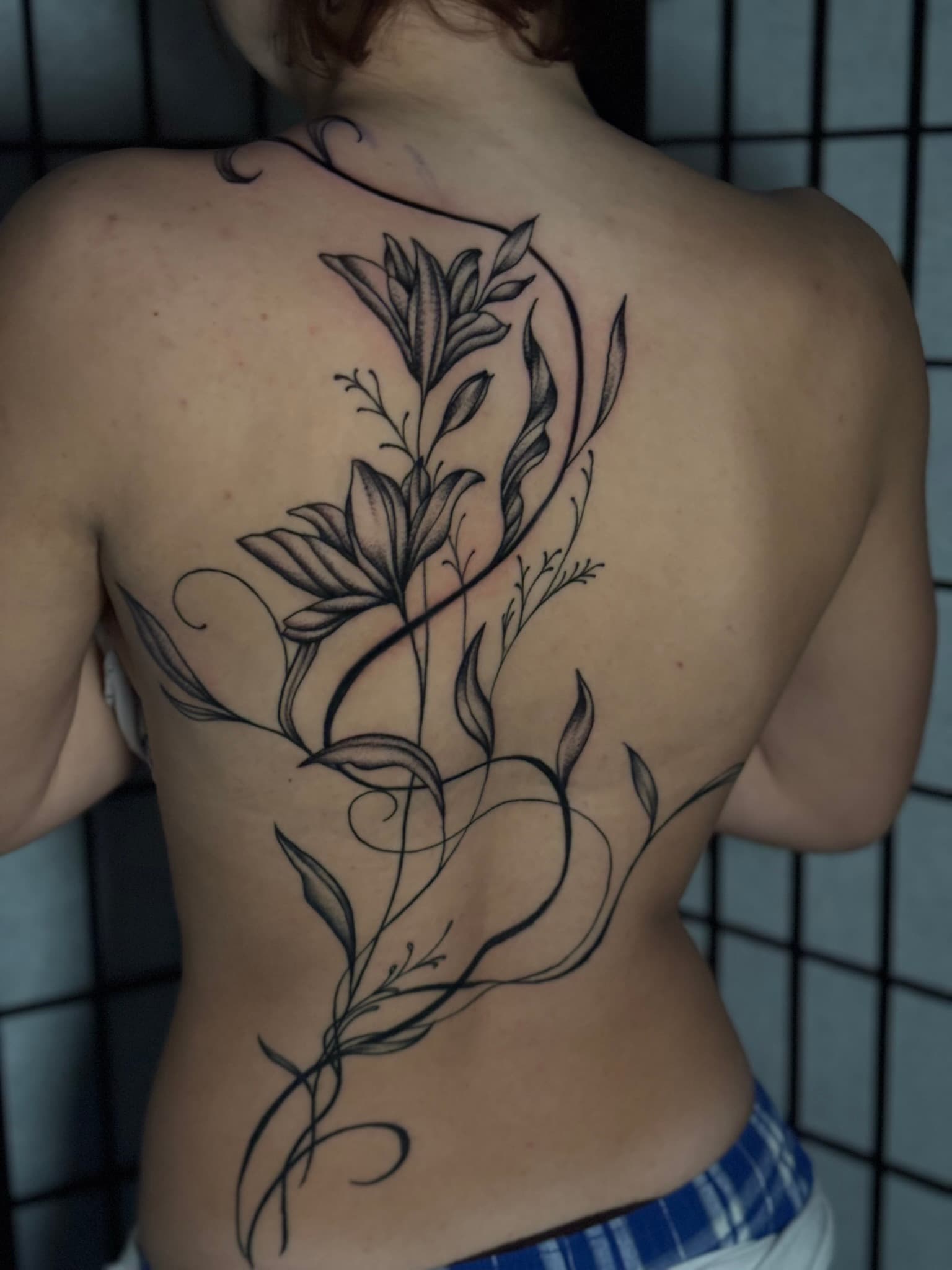 Fine line whimsical lilies back piece tattoo by Isaac Mackenzie, Oahu